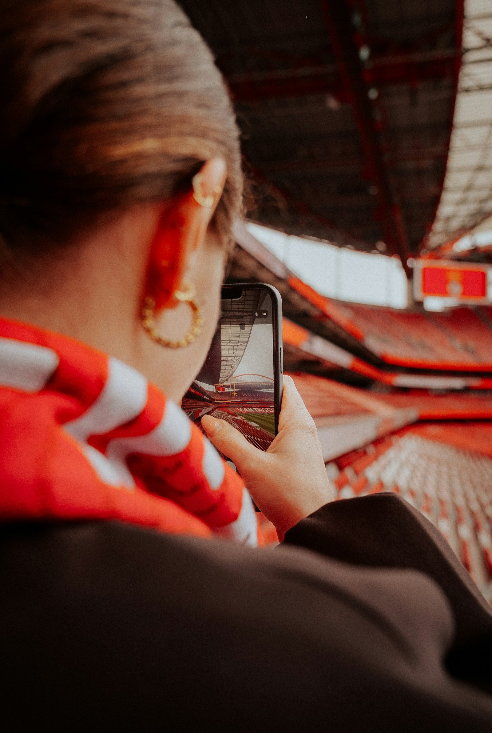 Látogató okostelefonnal fényképez egy modern futballstadionban.